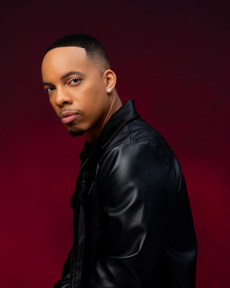 Vertical portrait of Jerel Crockett in a black leather jacket against a deep red backdrop.